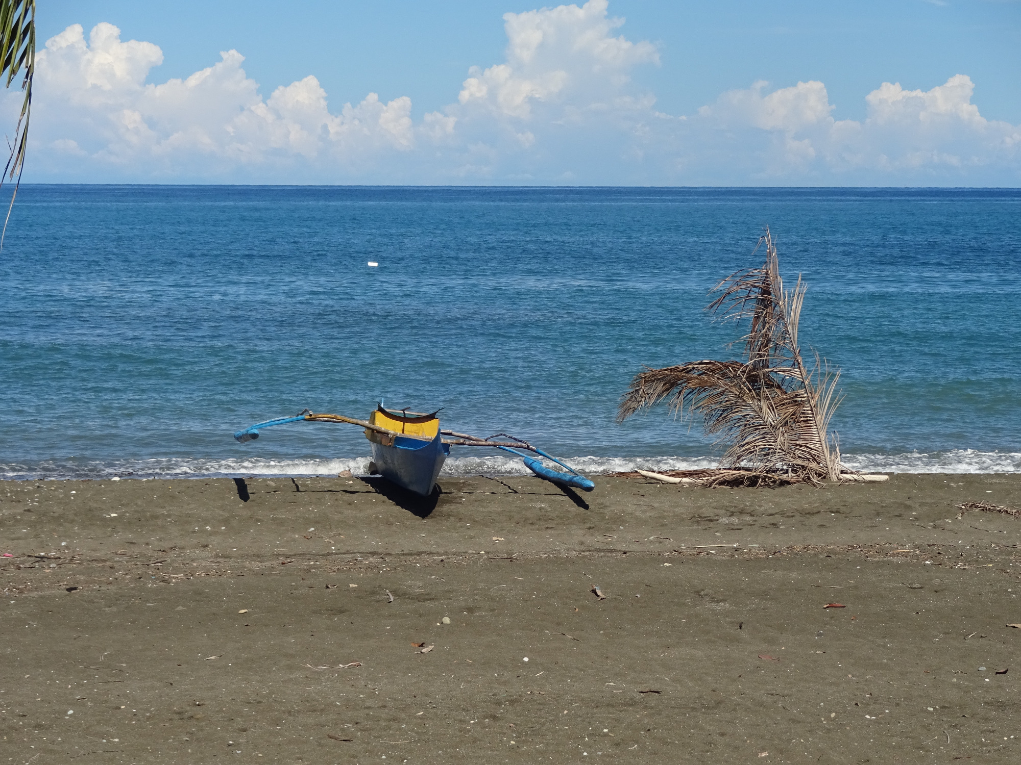 Auslegerboot am Strand vor blauem Meer – ein Reisemotiv