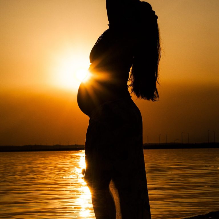 Schwangere im seitlichen Profil mit sichtbarem Babybauch im Sonnenuntergang